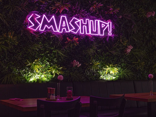 Angestrahlte, begrünte Wand mit der Leuchtschrift "SMASH UP!".
