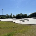 Skaterpark Much Moderner Skatepark mit Betonrampen und Geländern, umgeben von grünen Bäumen und Wiesen bei Sonnenschein.