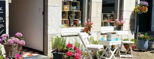 Steinfassade mit einem runden Tisch, zwei Stühlen und Blumenkästen davor.