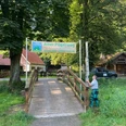 Banner Alter Pilgerweg im Haxtergrund Ein Holzsteg führt zu einem Schild des Alten Pilgerwegs im Haxtergrund, umgeben von Bäumen.
