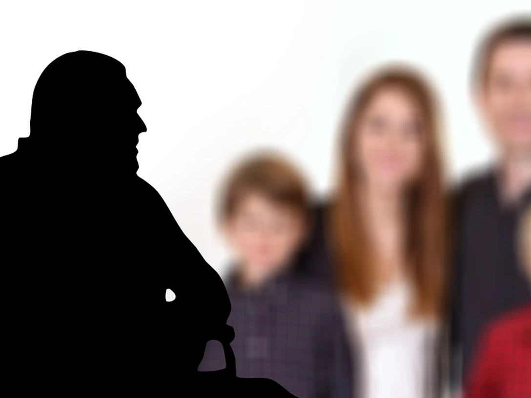 Demenz Ein Rollstuhlfahrer im Profil vor einer verschwommenen Familie im Hintergrund.