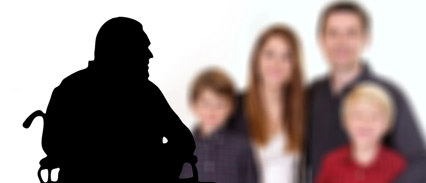 Demenz Ein Rollstuhlfahrer im Profil vor einer verschwommenen Familie im Hintergrund.