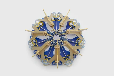Svenja John, brooch "NOKOMIS" Colorful brooch made of geometric elements arranged in a star shape on a grey background.