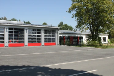 Feuerwehrgerätehaus Lashorst 2024 Feuerwehrgerätehaus mit modernen roten Toren, befestigtem Parkplatz und angrenzendem Grünbereich.