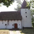 Weiße Kapelle mit markantem Satteldach und seitlichem Turm, umgeben von Bäumen und Natur.