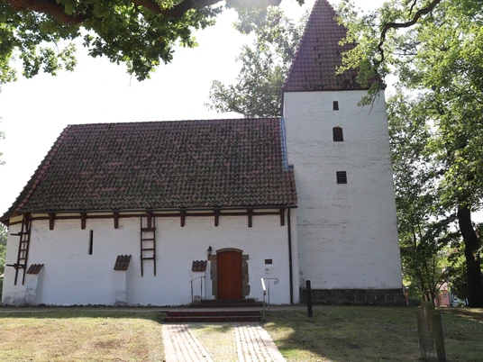 Kapelle Nordhemmern Weiße Kapelle mit markantem Satteldach und seitlichem Turm, umgeben von Bäumen und Natur.