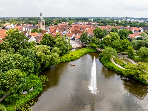 Luftaufnahme von Rheda-Wiedenbrück mit historischem Stadtkern, Kirchturm und zentralem Teichbrunnen.