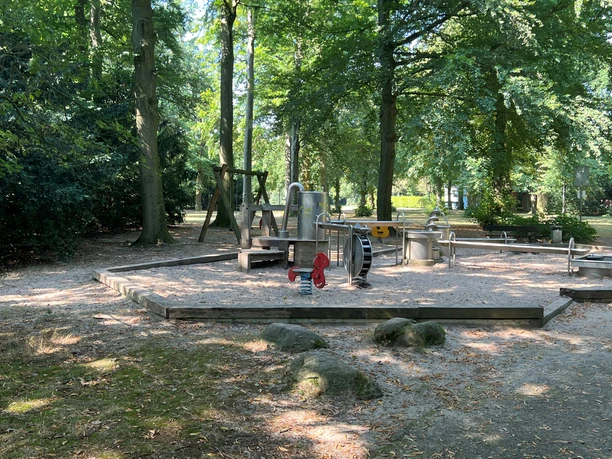 Wasserspielplatz im Bürgerpark mit Holzinstallationen, umgeben von schattenspendenden Bäumen.