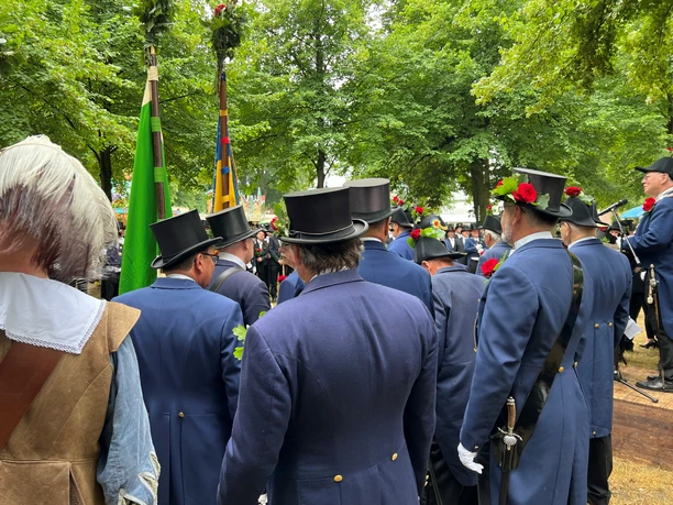 Scheibenschießen Teilnehmer eines traditionellen Schützenfests in Uniform und Zylinder mit Dekorationen, umgeben von Bäumen.