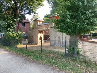 Spielplatz mit Holzklettergerüst und Rutschen, umgeben von Bäumen und Zäunen am Weserwall.