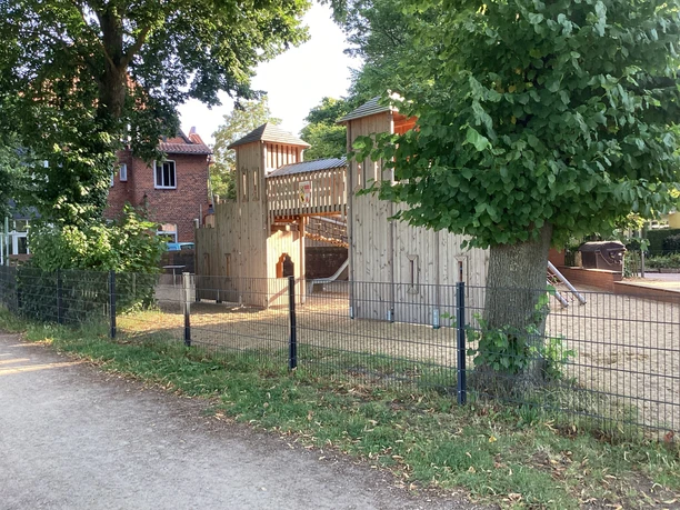Spielplatz am Weserwall Spielplatz mit Holzklettergerüst und Rutschen, umgeben von Bäumen und Zäunen am Weserwall.