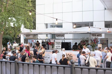 People are gathering at a bustling outdoor food stand.