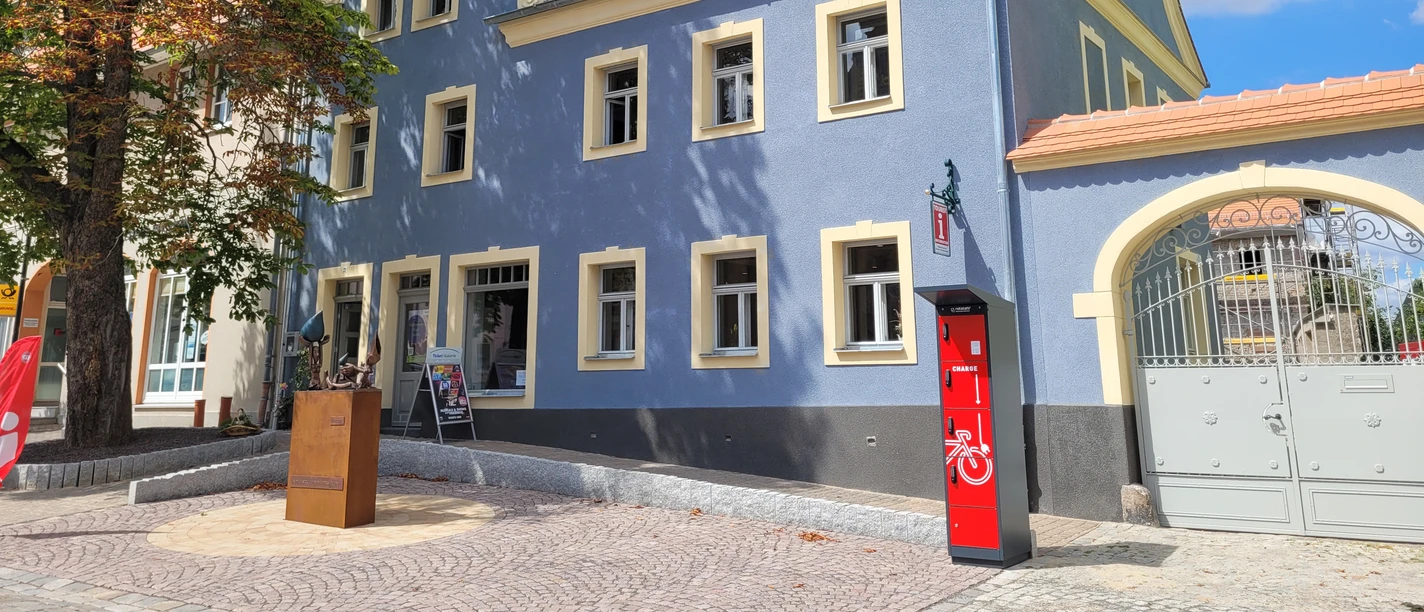 Tourist-Information Bad Lausick mit E-Bike Ladestation - Besucherberatung und Service Außenansicht der Touristinformation Bad Lausick, die Fassade ist leuchtend blau, auf der linken Seite des Eingangs steht eine Kastanie
