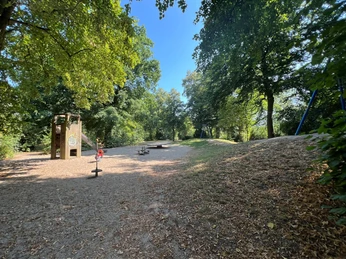 Wasserspielplatz Spielplatz mit Klettermöglichkeiten und Rutschen, eingebettet in schattenspendende Bäume.
