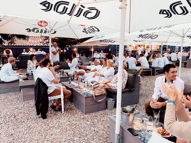 Kranenborgh Biergarten Menschen in heller Sommerkleidung genießen in einem lebendigen Biergarten unter großen Sonnenschirmen.