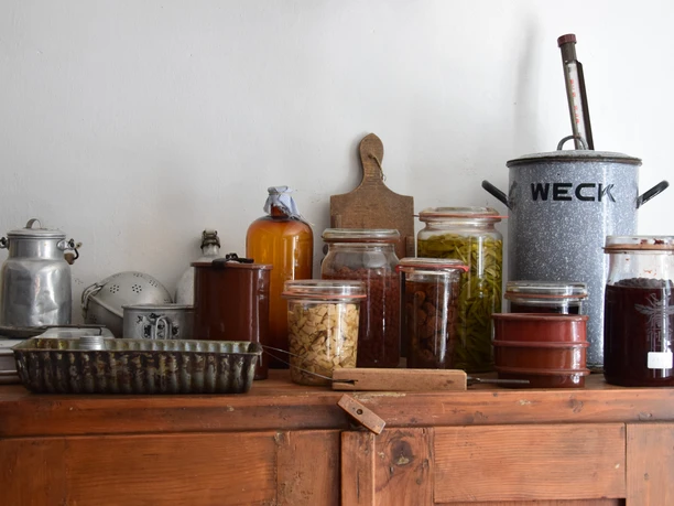 Bauernhofmuseum Ein rustikales Küchenregal mit Einmachgläsern, Saftkrügen und vintage Küchenutensilien.
