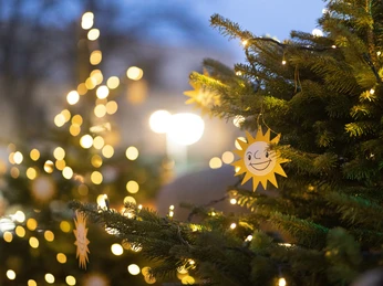 Weihnachtsmarkt mit leuchtenden Lichtern an geschmückten Tannenbäumen und fröhlichen Sonnendekorationen.