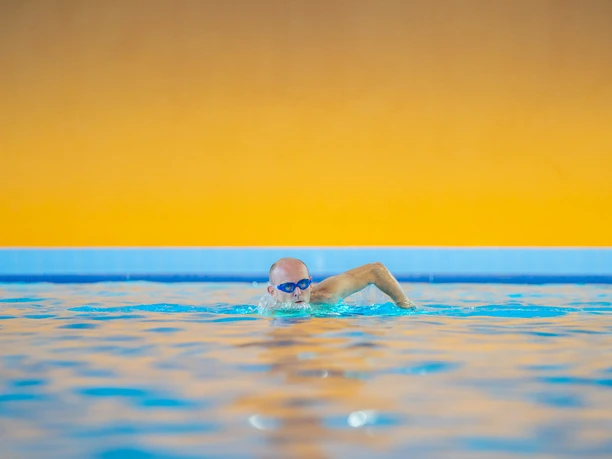 Erkrath Neanderbad Schwimmbecken Mensch beim Freistilschwimmen im blauen Schwimmbecken des Neanderbads vor orangefarbener Wand.