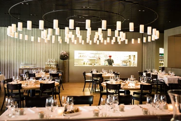 Dining room at Grill-Restaurant BAULÜÜT with set tables, pendant lights and open kitchen