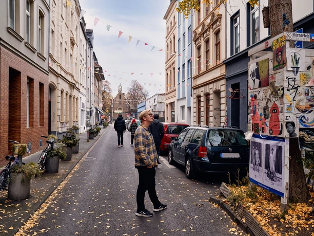 Körnerstraße Körnerstraße in Cologne-Ehrenfeld: Colorful houses, art posters on a tree, strolling passers-by.
