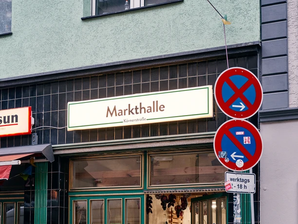 Körnerstraße An open door to the "market hall" with inviting shop windows, bicycles and street signs in front of it.