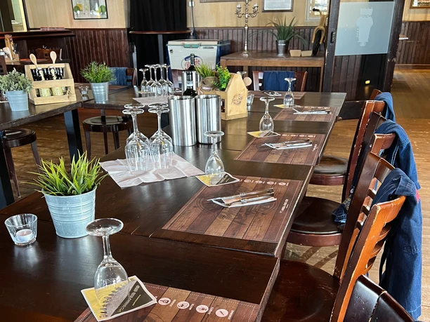 Grillkurs im Road Stop Mettmann Ein festlich gedeckter Holztisch mit Weingläsern und Tischset in einem rustikalen Speiseraum.