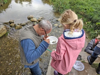 Explorer les micro-organismes Ein Mann untersucht den Inhalt einer weissen Plastikschale, ein blondes Mädchen schaut ihm dabei zu A man examines the contents of a white plastic bowl while a blonde girl watches himUn homme examine le contenu d'une barquette en plastique blanc, une jeune fille blonde l'observe.