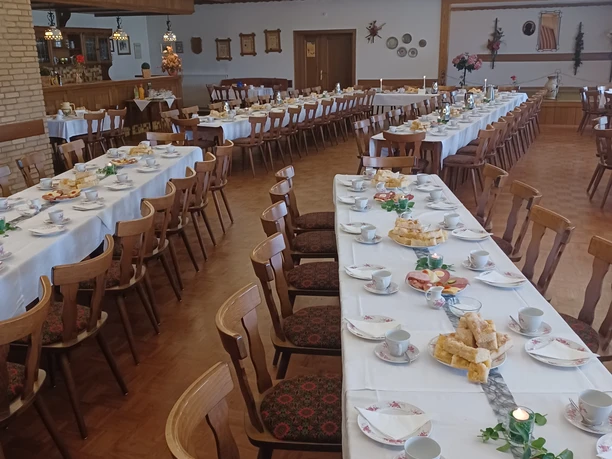 A festively decorated hall with long tables, wooden chairs and table decorations for a celebration.