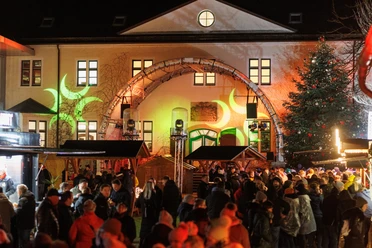 Menschenmenge auf belebtem Weihnachtsmarkt vor beleuchtetem historischen Gebäude bei Nacht.