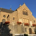 Kirche Bad Holzhausen.JPG Ein steinernes Kirchengebäude mit Blumen geschmückt, im Sonnenlicht einer klaren, blauen Tageszeit.