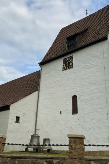 St. UlricusTouristik Preußisch Oldendorf.jpg Weiße Kirche mit Satteldach und Turm, umgeben von einer niedrigen Steinmauer und Bäumen.
