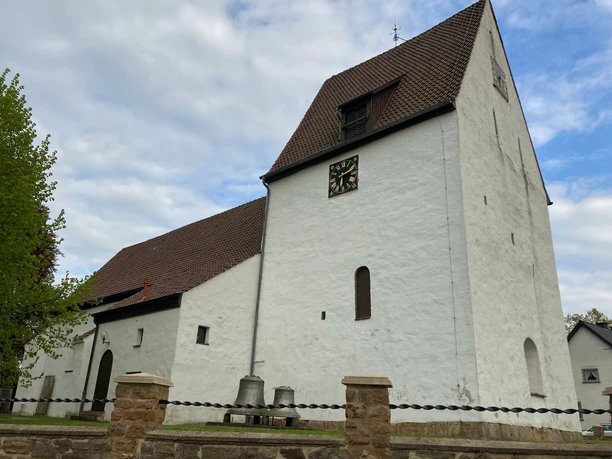 St. UlricusTouristik Preußisch Oldendorf.jpg Weiße Kirche mit Satteldach und Turm, umgeben von einer niedrigen Steinmauer und Bäumen.