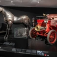 Cologne City Museum Depiction of a historic automobile next to a metal horse sculpture in the Cologne City Museum.