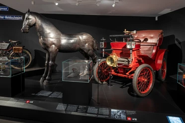 Kölnisches Stadtmuseum Darstellung eines historischen Automobils neben einer metallischen Pferdeskulptur im Kölner Stadtmuseum.