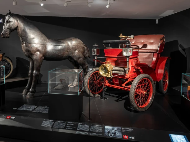 Kölnisches Stadtmuseum Darstellung eines historischen Automobils neben einer metallischen Pferdeskulptur im Kölner Stadtmuseum.