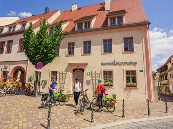Tourist Information Wurzen am Markt Vor der Tourist-Information im gelben Fachwerkhaus rasten drei Radfahrer*innen