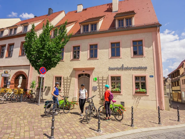 Tři cyklisté odpočívají před turistickým informačním centrem ve žlutém hrázděném domě.
