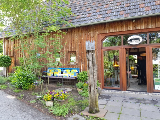 Galerie Sattelgut Gemütliches Fachwerkgebäude mit Holzdach und großen Fenstern, umgeben von grüner Vegetation.