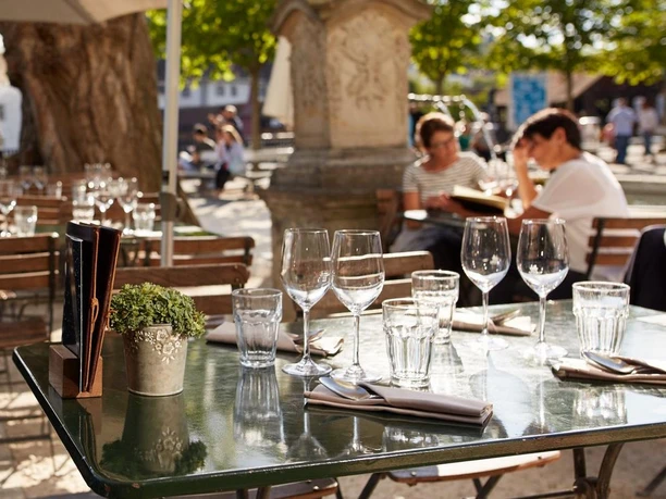 Sunlit Mill'Feuille terrace with set tables and guests beneath trees in Lucerne