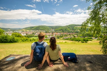 l-gde-osterberg-teutoburger-wald-tourismus-d-ketz-057-jpg.jpg Zwei Personen sitzen auf einer Bank und blicken auf die grüne Landschaft und die Stadt im Teutoburger Wald.