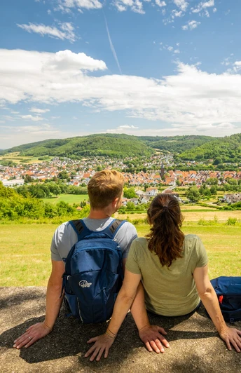 l-gde-osterberg-teutoburger-wald-tourismus-d-ketz-057-jpg.jpg Zwei Personen sitzen auf einer Bank und blicken auf die grüne Landschaft und die Stadt im Teutoburger Wald.