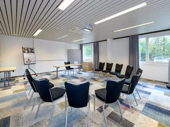 Tagungsraum Tagungsraum mit Stuhlkreis, Leinwand und TageslichtMeeting room with a circle of chairs, a screen and daylight