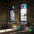 Stadt Petershagen_Petershagen_Evelyn Hotze_Alte Synagoge_Innenraum_Vitrinen_Spiegelung bunte Fenster_Sonne_quer.jpg Innenraum einer Synagoge mit Vitrinen und farbigen Glasfenstern, Sonnenstrahlen erzeugen bunte Reflexionen.