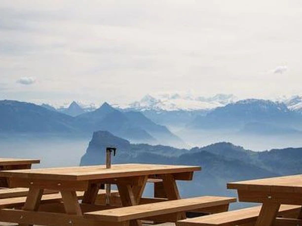 Holztische auf der Drachenalp-Terrasse mit weitem Blick auf Berge und Vierwaldstättersee