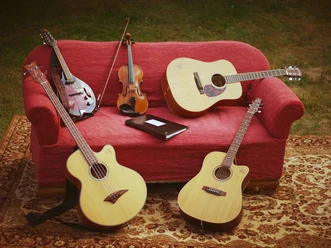 Fünf Saiteninstrumente ruhen auf einem roten Sofa im Freien, darunter Gitarren und eine Geige.