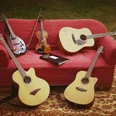 JamSession_Instrumente_800.jpg Fünf Saiteninstrumente ruhen auf einem roten Sofa im Freien, darunter Gitarren und eine Geige.