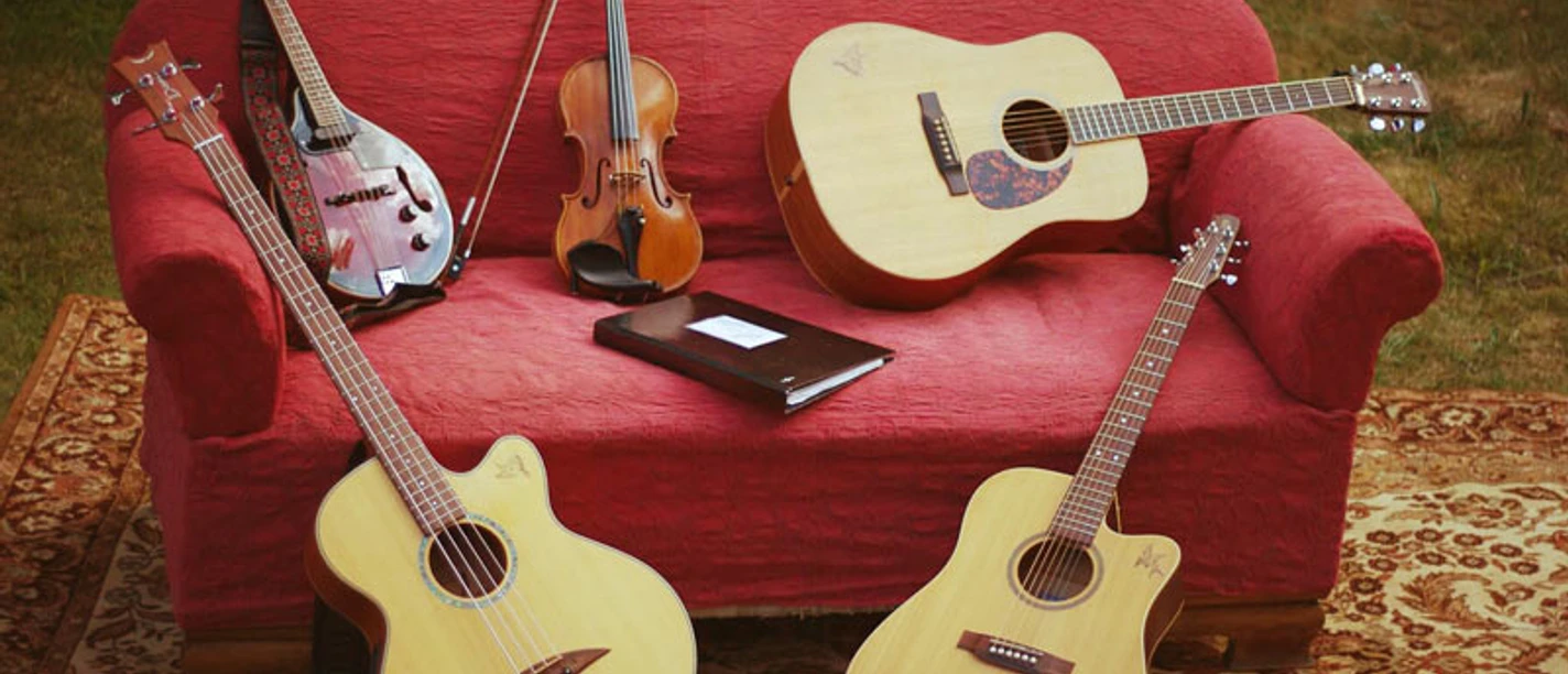 JamSession_Instrumente_800.jpg Fünf Saiteninstrumente ruhen auf einem roten Sofa im Freien, darunter Gitarren und eine Geige.
