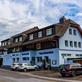 Haus Rheinblick Ott, Monheim am Rhein Dreistöckiges Gästehaus mit Parkmöglichkeiten, blau-weißer Fassade und Eifeler-Landbier-Schild.