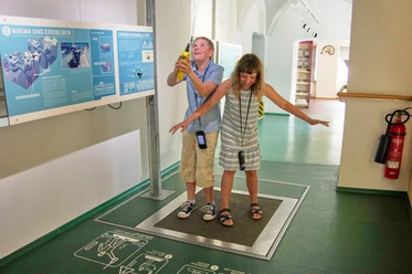 Erdbeben Zwei Kinder stehen auf einer Plattform in einem Museum und simulieren ein Erdbeben.