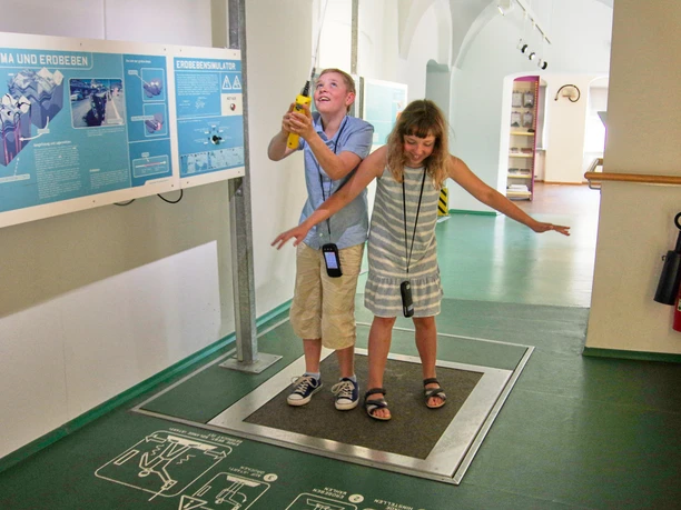 Erdbeben Zwei Kinder stehen auf einer Plattform in einem Museum und simulieren ein Erdbeben.